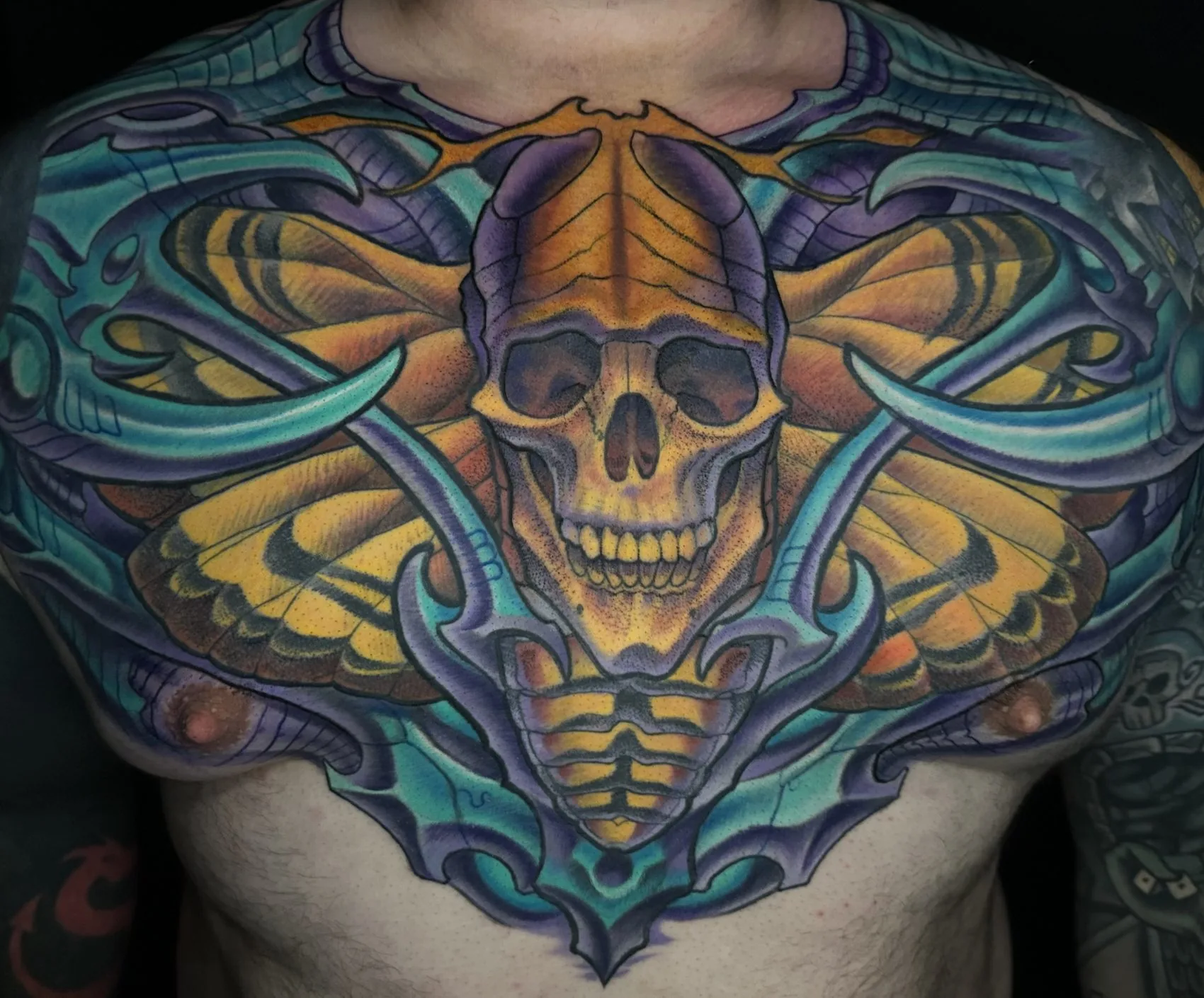 Bio-organic full color chest piece tattoo of a moth with a skull thorax in yellow, purple and teal by Terry Ribera at Remington Tattoo in San Diego.