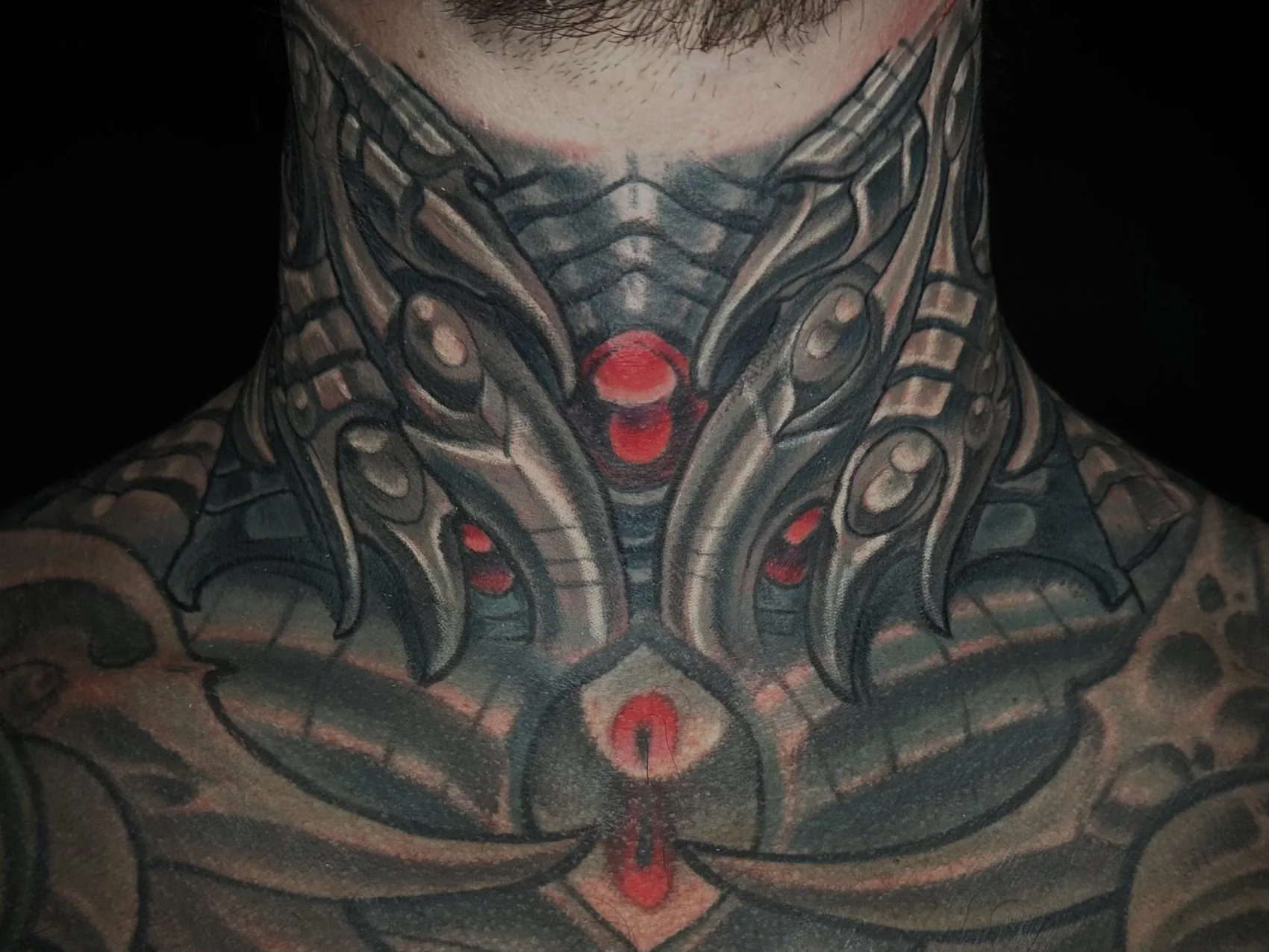 Biomechanical tattoo across the front of the throat and down onto the collarbones and upper chest by Terry Ribera at Remington Tattoo in San Diego.