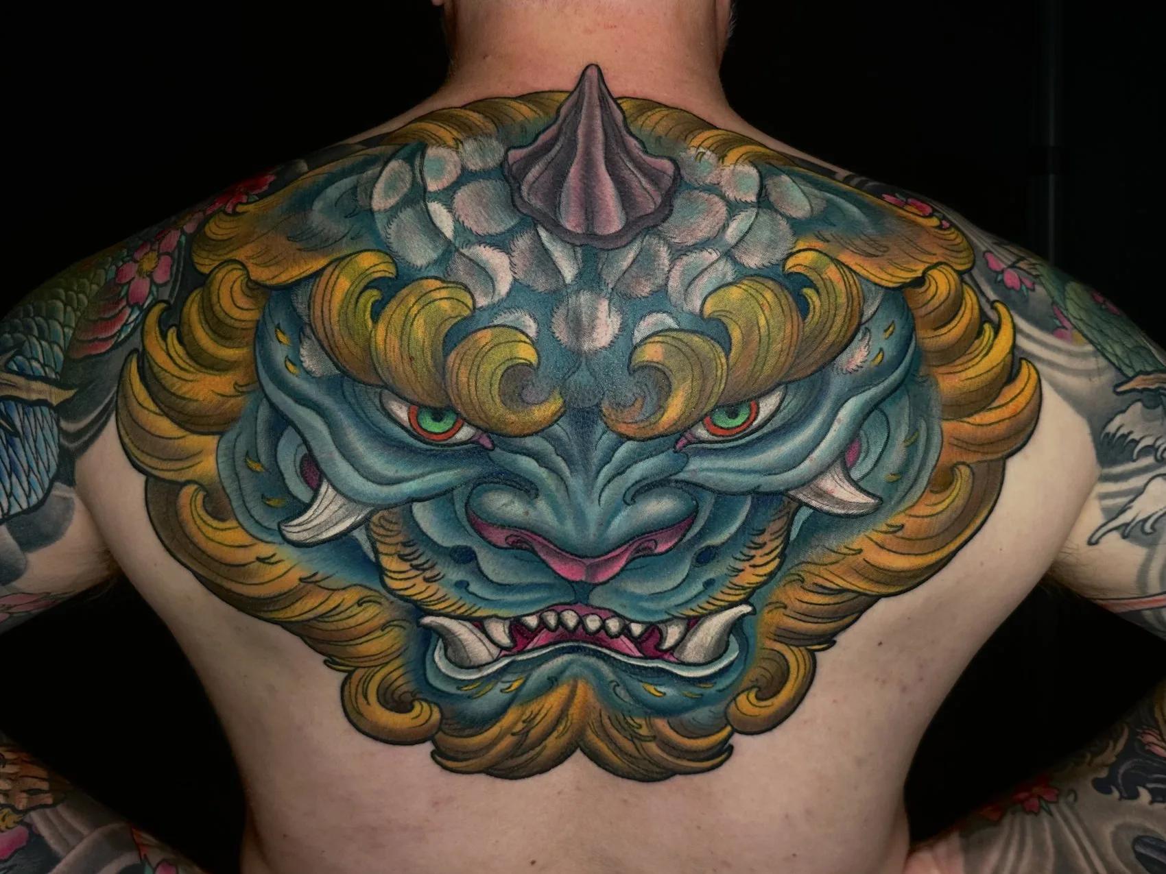 Neo Japanese full color upper back tattoo of a blue foo dog with gold mane by Terry Ribera at Remington Tattoo in San Diego.