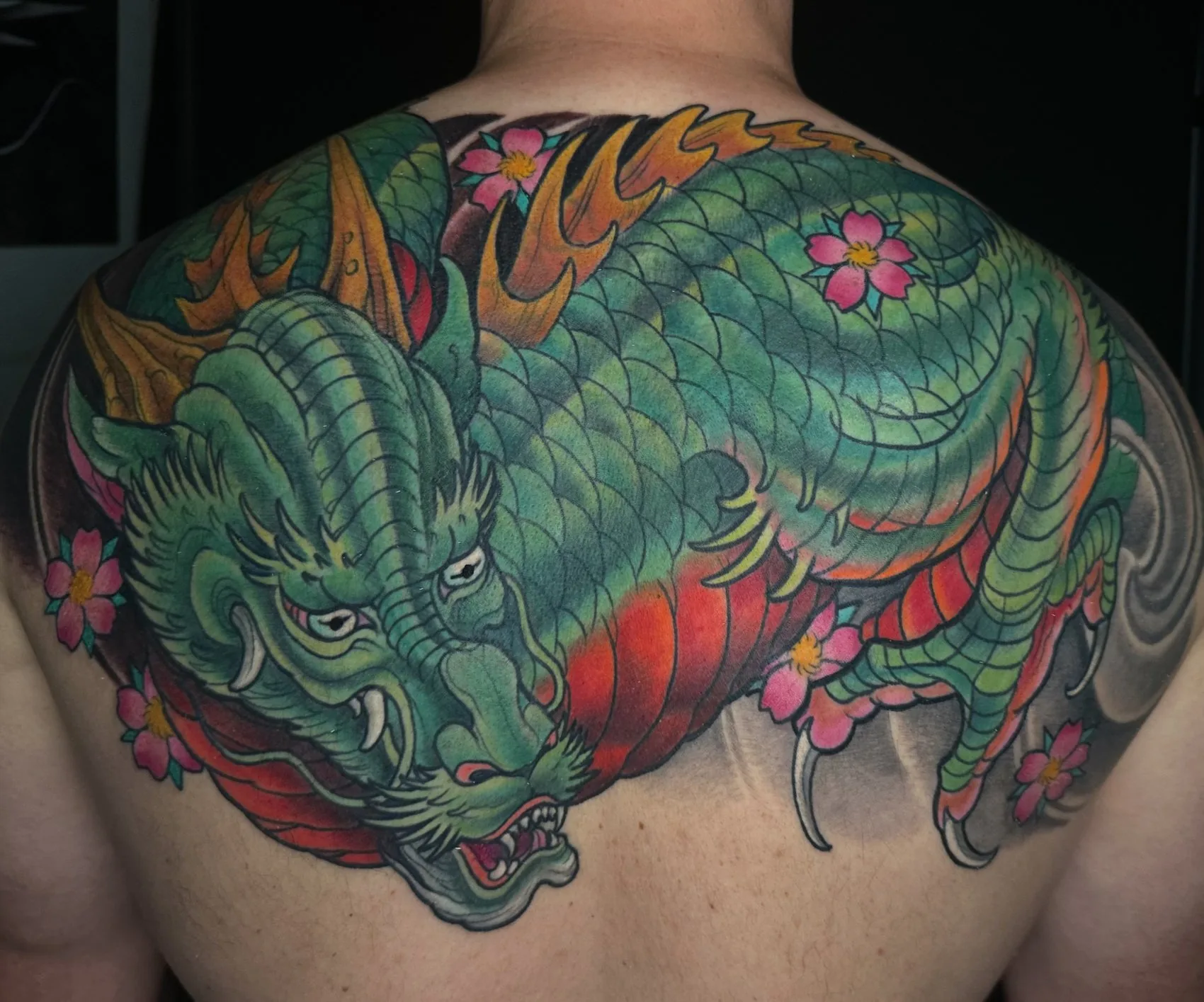 Neo Japanese full color upper back tattoo of a green dragon with cherry blossoms and flame by Terry Ribera at Remington Tattoo in San Diego.