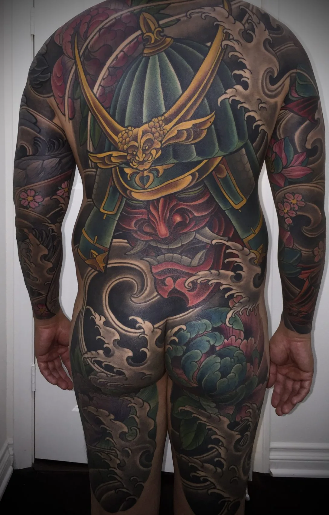 Neo Japanese bodysuit tattoo, rear view of a samurai helmet and hannya mask back piece flowing into both arm sleeves and down over the buttocks and thighs by Terry Ribera at Remington Tattoo in San Diego.