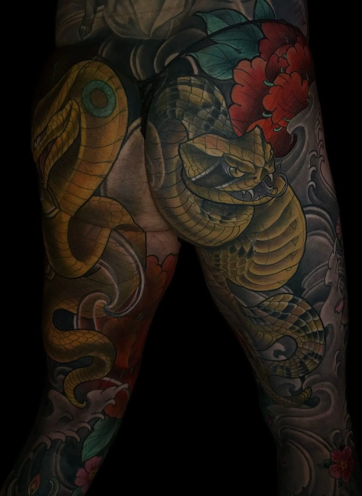 Neo Japanese tattoo showing both thighs and buttocks with two snakes and peonies over black-and-grey waves by Terry Ribera at Remington Tattoo in San Diego.
