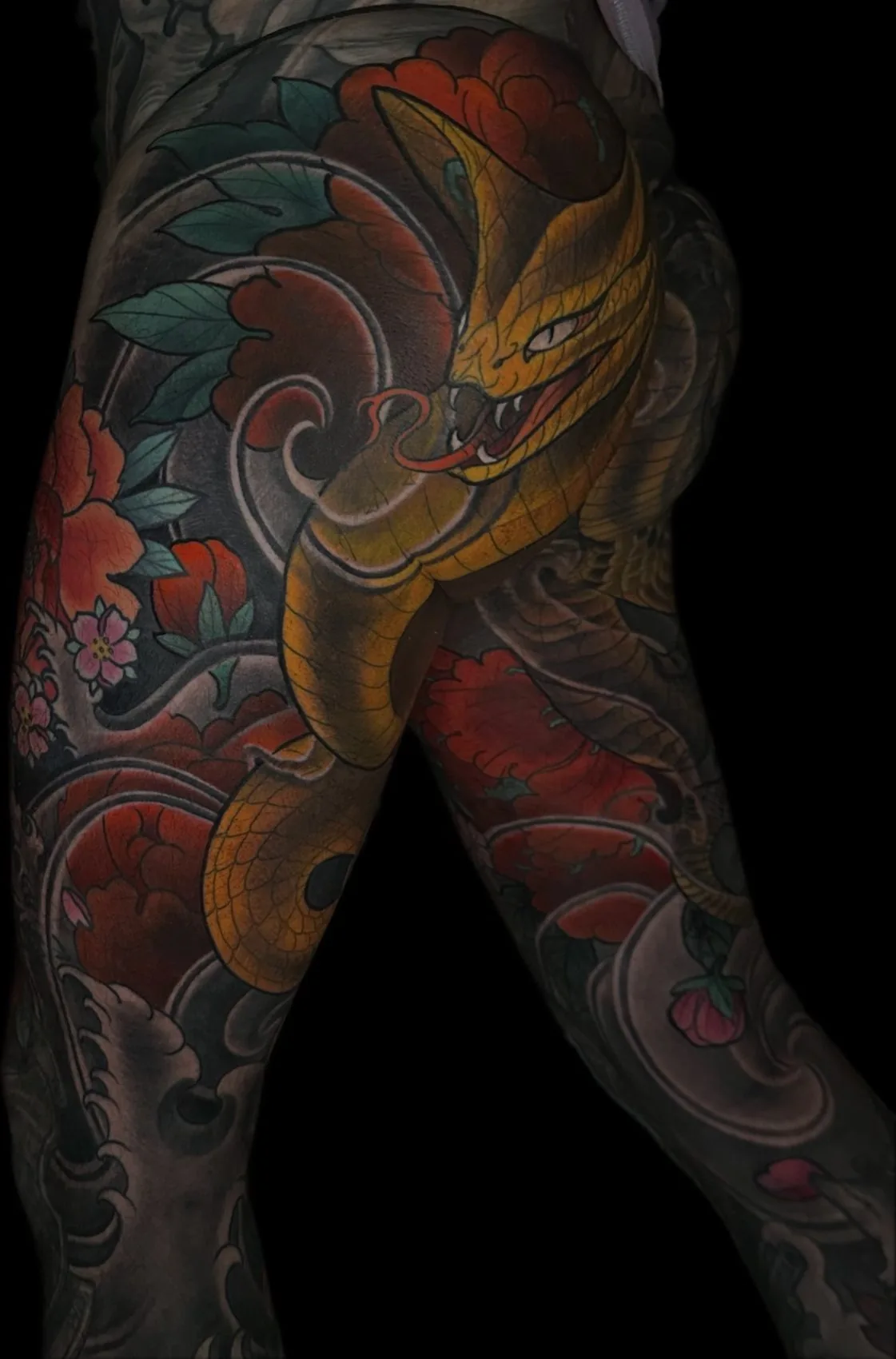 Neo Japanese tattoo of a yellow snake among red peonies across the back of the thigh and buttock by Terry Ribera at Remington Tattoo in San Diego.