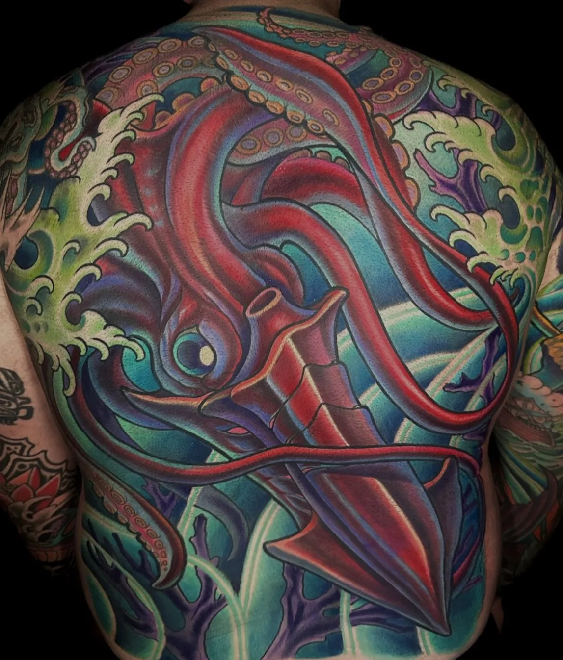 Full color back piece tattoo of a giant red squid among green waves and coral by Terry Ribera at Remington Tattoo in San Diego.