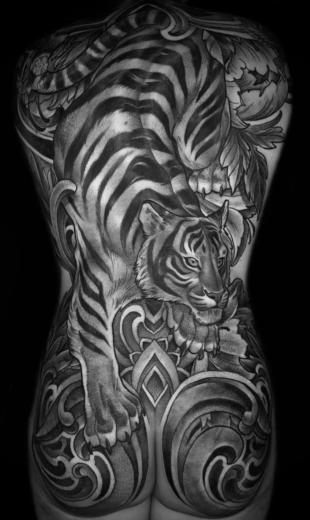 Black and grey back piece tattoo of a crouching tiger with ornamental scrollwork continuing over the buttocks by Terry Ribera at Remington Tattoo in San Diego.