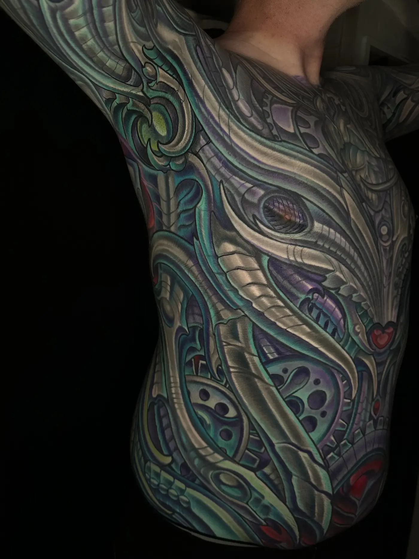 Biomechanical side torso tattoo in teal and silver flowing continuously from arm to waist, body suit section by Terry Ribera San Diego